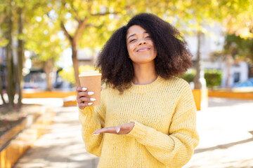 pretty afro black woman smiling cheerfully, feeling happy and showing a concept. take away coffee...