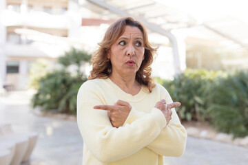 middle age woman looking puzzled and confused, insecure and pointing in opposite directions with doubts