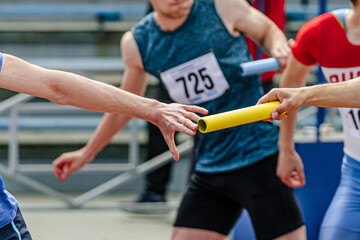men relay race baton passing in summer athletics championship, close-up of athletes hands on background of runners - obrazy, fototapety, plakaty