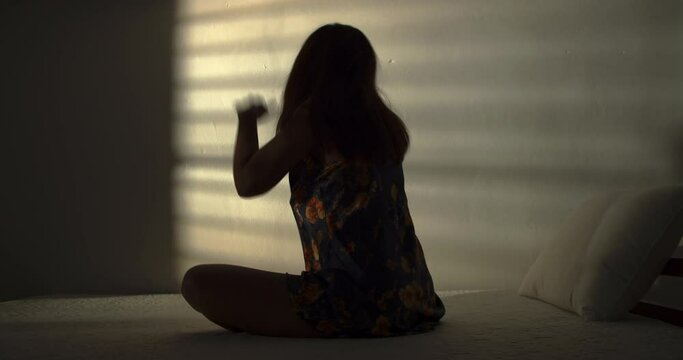 A lonely woman is sitting on the bed in a narrow dark room. This concept use for symptoms of stress, major depressive disorder (MDD), psychotic symptoms.