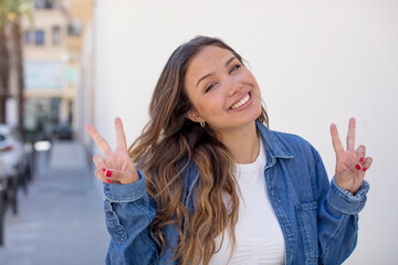 pretty hispanic woman smiling and looking happy, friendly and satisfied, gesturing victory or peace with both hands