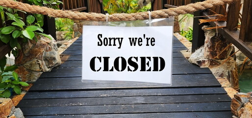 sorry we're closed. Label in white paper sign printed in black ink hangs in a rope on a wooden...