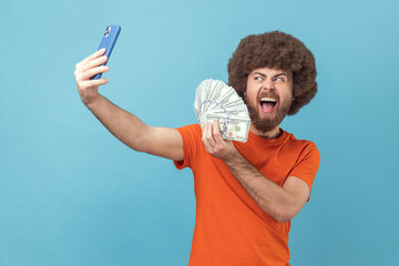 Portrait of excited man with Afro hairstyle wearing orange T-shirt having video call or livestream,...