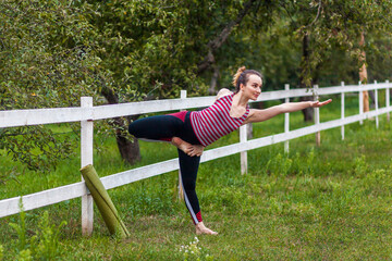 Full length portrait of young sporty attractive woman wearing sportswear practicing yoga, doing Natarajasana exercise, Lord of the Dance pose, working out in park with beautiful nature.