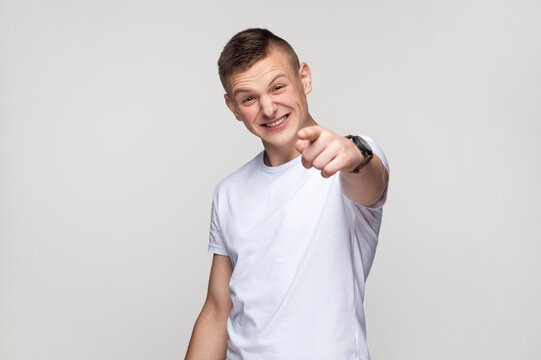 Portrait of happy laughing young teenager boy wearing T-shirt looking at camera with toothy smile, pointing at camera with finger, laugh at you. Indoor studio shot isolated on gray background.