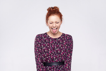 Portrait of naughty playful ginger woman with bun hairstyle wearing dress showing tongue at camera...