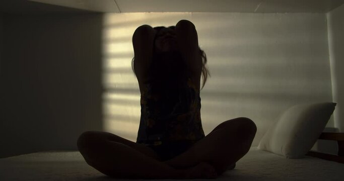 A lonely woman is sitting on the bed in a narrow dark room. This concept use for symptoms of stress, major depressive disorder (MDD), psychotic symptoms.