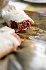 Close up of a recently cooked meat tamale cut in half on top of a plant leaf