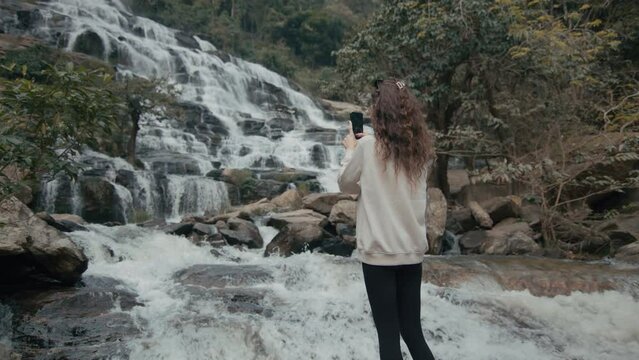 A young woman takes a picture of a majestic waterfall in northern Thailand