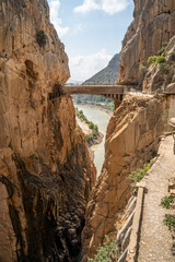 Group of people with protection helmet doing the Caminito del Rey in Malaga, walking through a ferrata route during a sunny summer day
