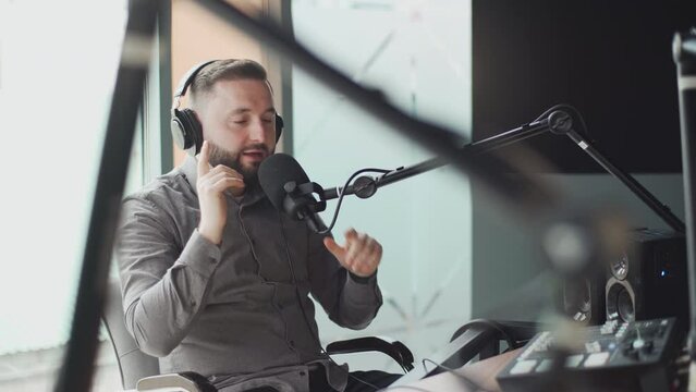 Handsome radio host is preparing to broadcast on a radio show and puts on headphones. Shows a kiss to the camera.
