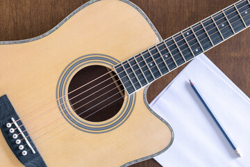 Obraz premium Guitar, sheet of paper and pencil on a wooden background, top view.