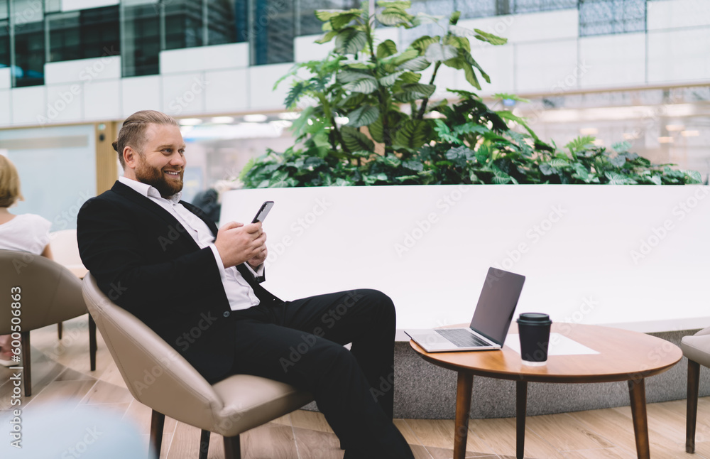 Poster smiling businessman resting in outside cafe and using smartphone