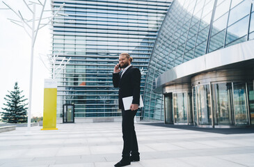 Fototapeta na wymiar Positive businessman talking on smartphone over modern office building