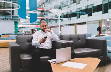 Focused man using smartphone while resting on sofa