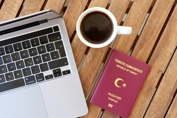 Turkish passport with coffee cup and laptop on wooden table photographed from above