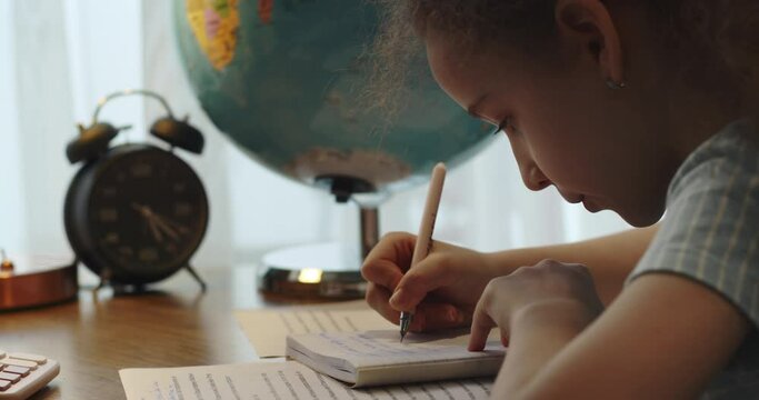 Cute smart primary school child girl learning writing doing math homework sit at home table, adorable pretty little preschool kid studying alone making notes, children elementary education concept