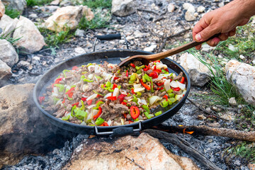 man prepares food on a campfire in a clearing near the mountains. Stalker, survive in the jungle