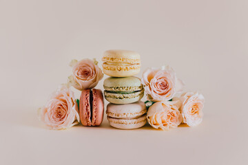 Obraz na płótnie Canvas Tasty french macarons with tender rose flowers on a peach pastel background.