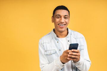 Smiling african american young man holding phone isolated on yellow studio background with copy space aside, african guy using mobile applications, texting.