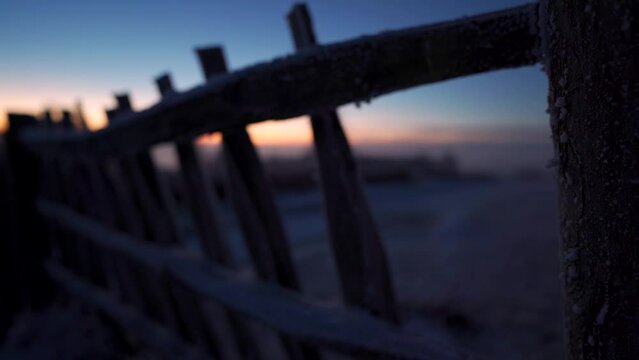 Abstract shot of a person walking past a frozen wooden fence at dawn