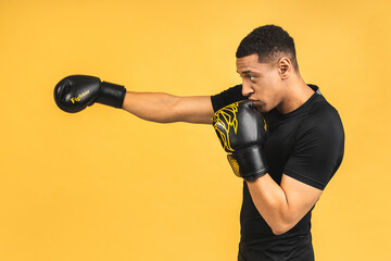 Angry Fighter. Aggressive young african american sports man in boxing gloves isolated over yellow background.