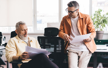 Confident financial experts discussing business documents during working time in office interior,...