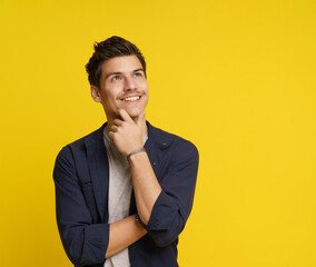 Fototapeta premium Young man in a thoughtful pose, with smile on his face, lost in his dreams and aspirations. Shot on yellow background, conveys sense of creativity and inspiration, highlighting his unique