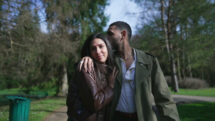 A Middle Eastern couple wrapped in love, strolling outdoors in a park with beaming smiles and...