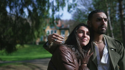 A Middle Eastern couple wrapped in love, strolling outdoors in a park with beaming smiles and affectionate embrace during a beautiful sunny day