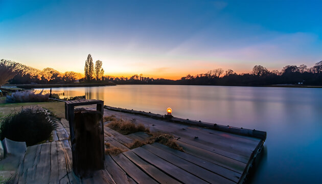 Sunset over a lake with a wooden jetty and a small house. AI generated image