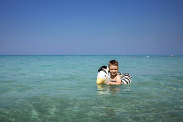 A boy swims, a child with an inflatable lifebuoy in the shape of a zebra. Summer swim. Bathing a child in water. Active sea recreation. Summer swimming, travel. Bathing a child in water