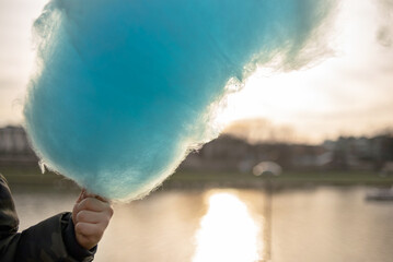 The hands of a child holding a blue cotton candy in the background of the sky