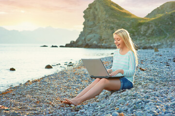 Technology and travel. Working outdoors. Freelance concept. Pretty young woman using laptop on the beach.