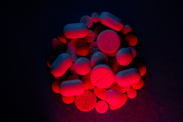 Extasy and drug concept. Close up shot of white and colored pills of different kind lit with red and blue neon lights.