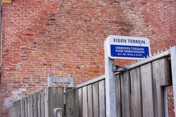 Dutch blue private property sign with in the background a stone wall and a fence with barbed wire....
