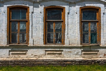 The wall of a village house made of bricks painted with white lime with three old windows covered with tulle curtains on a sunny spring day
