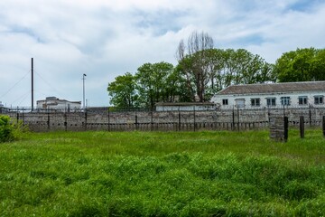 buildings of an abandoned prison for criminals behind a fence overgrown with green grass in the south of Russia on a sunny spring day.