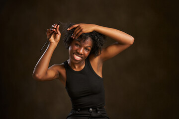 Young happy ethnic girl with afro hairstyle untangling her hair