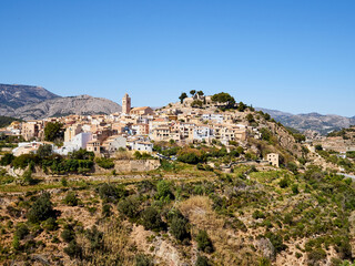 Fototapeta na wymiar View of the church of San Pedro (St. Peter), the city wall, the houses and the castle on the hill in Polop de la Marina, a picturesque village in Marina Baixa, Alicante, Valencian Community, Spain