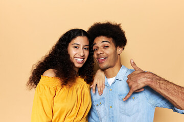 Obraz premium Lovely young african american couple posing against brown background, female leaning her hand on male's shoulder, smiling while guy showing tongue and give me a call gesture with hand and fingers