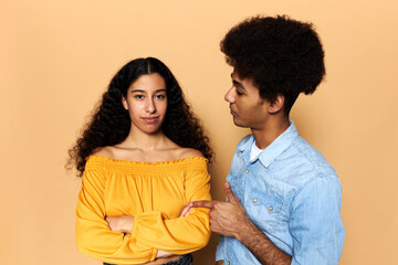 Dissatisfied boyfriend pointing at his girlfriend, accusing her, blaming for mistakes, girl with dark skin and long hair looking at camera with folded arms, ignoring his annoying speech