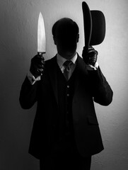 Portrait of Shadow Man in Dark Suit Holding Bowler Hat and Sharp Knife. Concept of Horror Killer