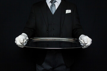 Portrait of Elegant Butler in Dark Suit and White Gloves Holding Large Silver Serving Tray. Service Industry and Professional Hospitality. - obrazy, fototapety, plakaty