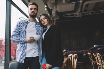 Trendy young romantic couple chilling in cozy cafe and looking at camera