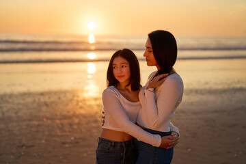 portrait latina mother and daughter embraced showing love to each other on the beach at sunset