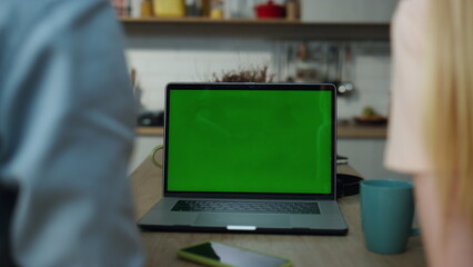 Couple watching green screen laptop sitting at kitchen table with coffee closeup
