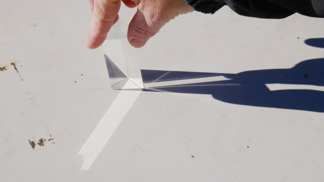 Hand moving a triangular prism in full sunlight and creating the refraction and decomposition of sunlight in the colors of the rainbow on a rusty white metal plate
