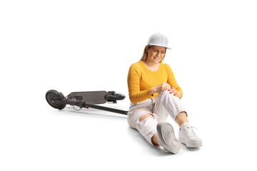 Young female with a scooter sitting on the floor and holding her painful knee