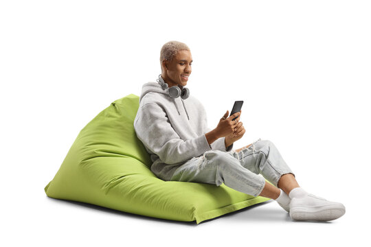African american young man seated on a bean bag smiling and looking at a mobile phone